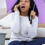 woman holding umbrella in her home on phone with roofing company for leak