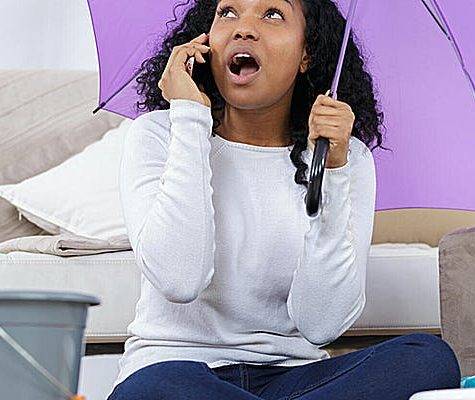 woman holding umbrella in her home on phone with roofing company for leak