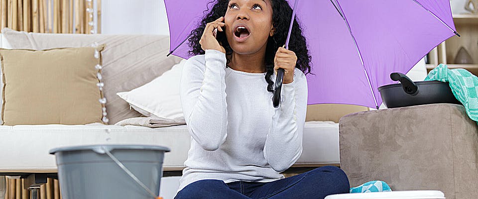 woman holding umbrella in her home on phone with roofing company for leak